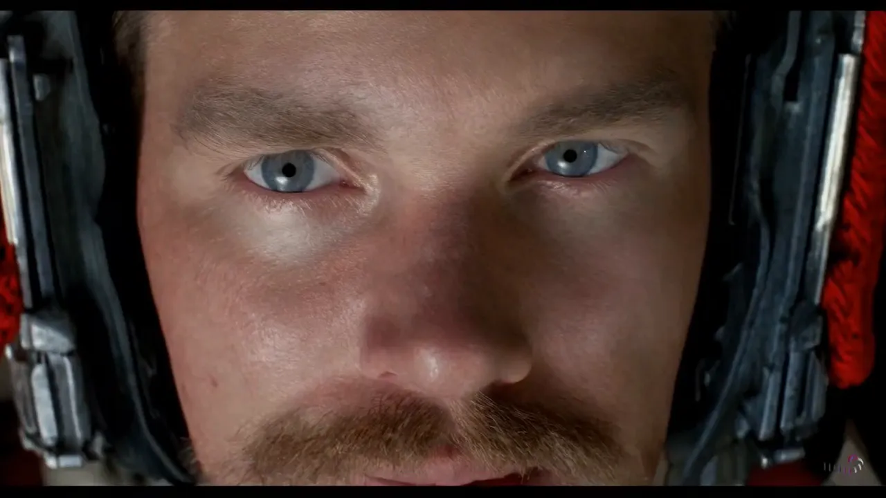 Close-up of an astronaut's blue-eyed face framed by the padded interior of a helmet.